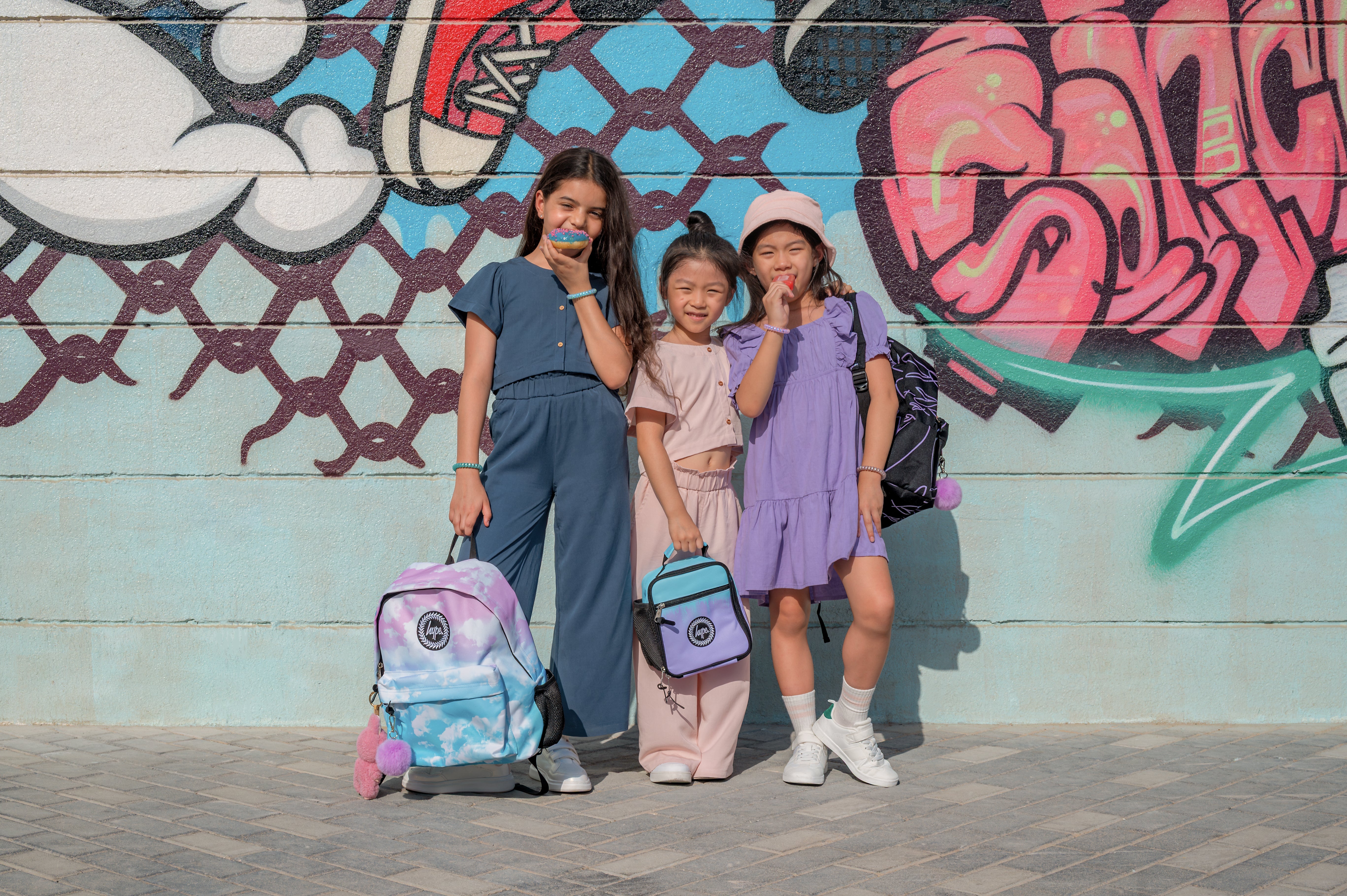 Kids wearing HYPE backpacks posing against graffiti wall in Dubai, showcasing UAE streetwear style 2025.