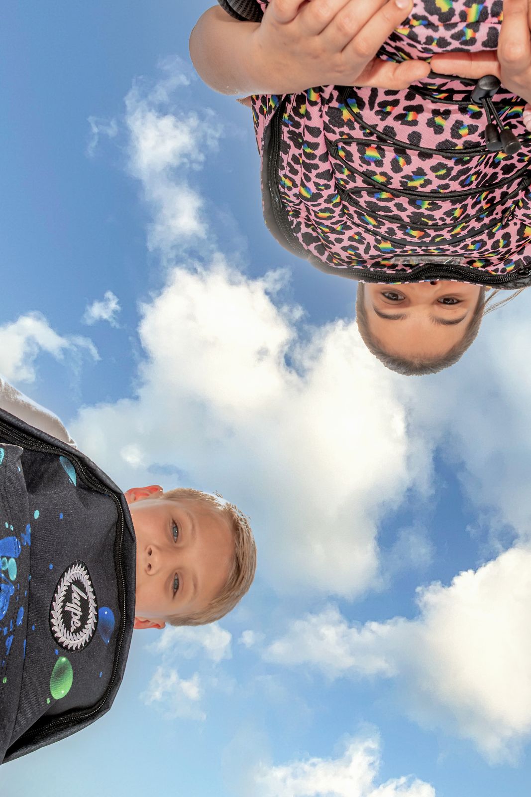 two kids wearing streetwear backpacks looking down outdoors